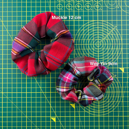 Two tartan scrunchies on a cutting mat showing the sizes: the larger Muckle (12 cm) and the smaller Wee Yin (9 cm).